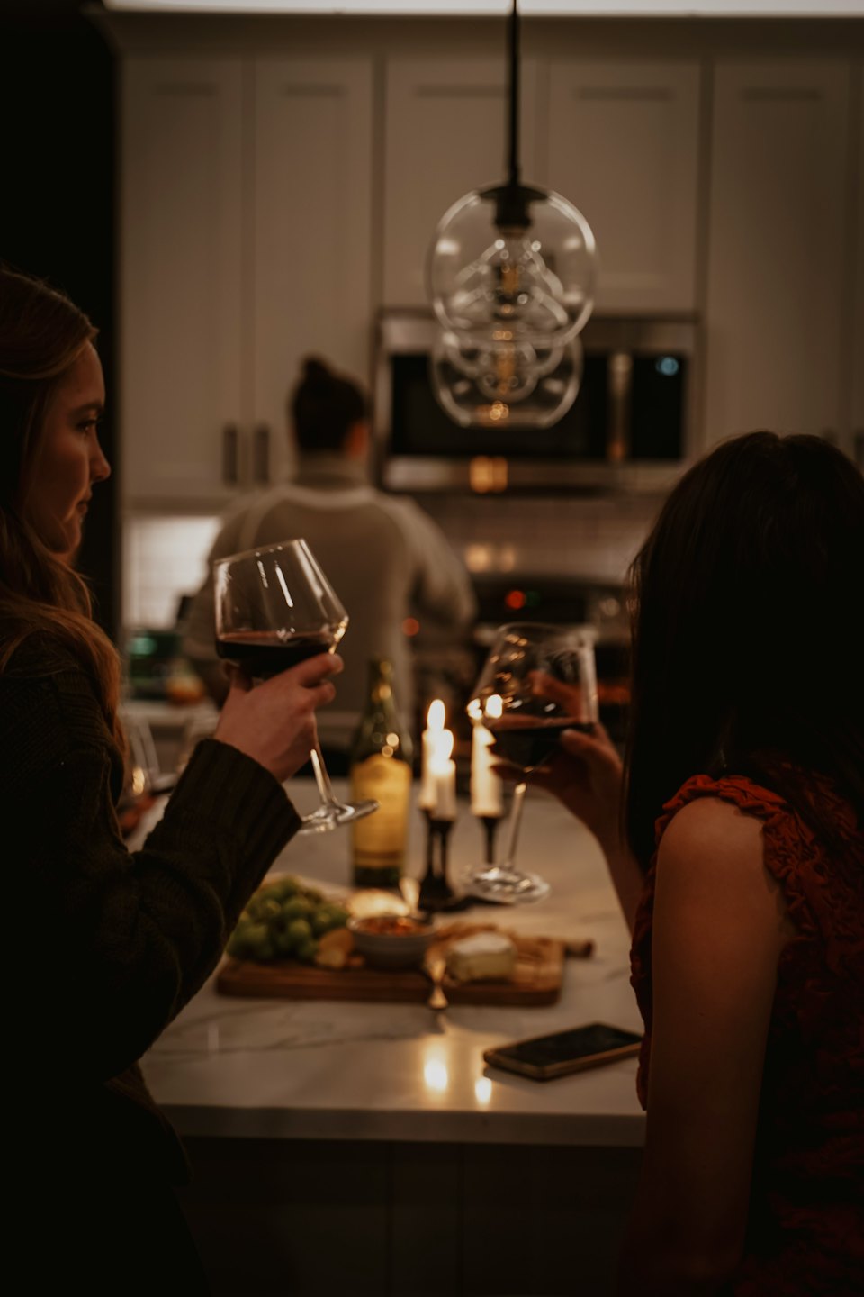 Two women toast with red wine in a modern kitchen.